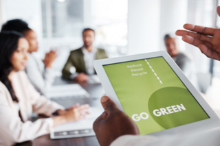 group of people in conference room with focus on an iPad with a presentation about going green